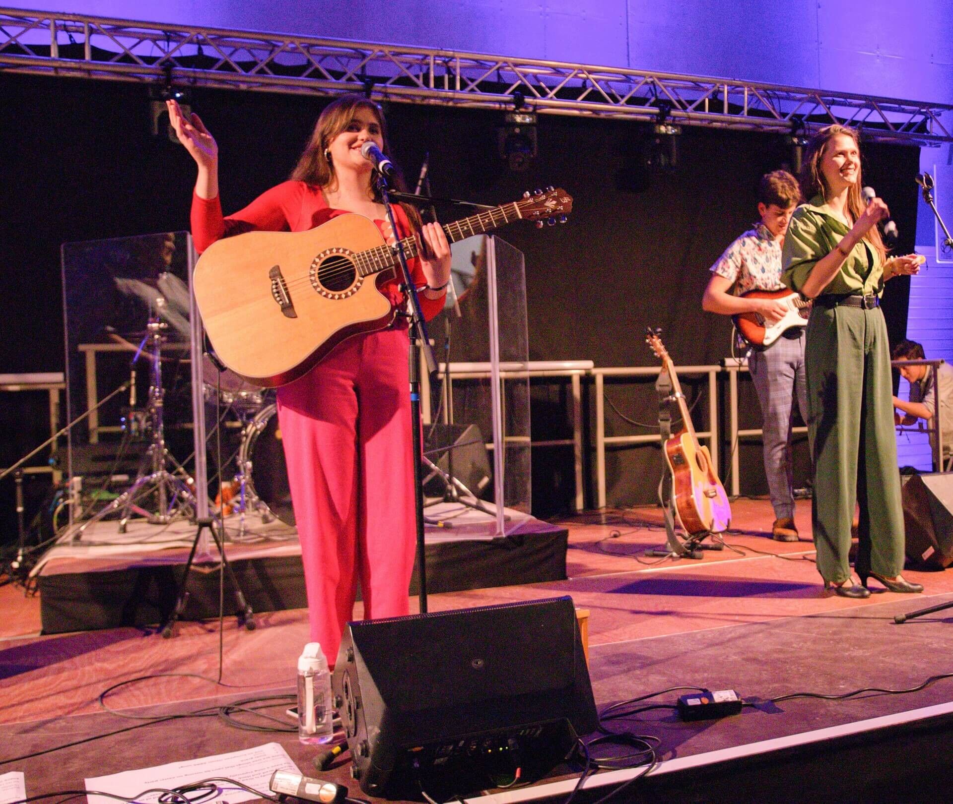 The Rejoice band on stage under purple light, a singer with an acoustic guitar