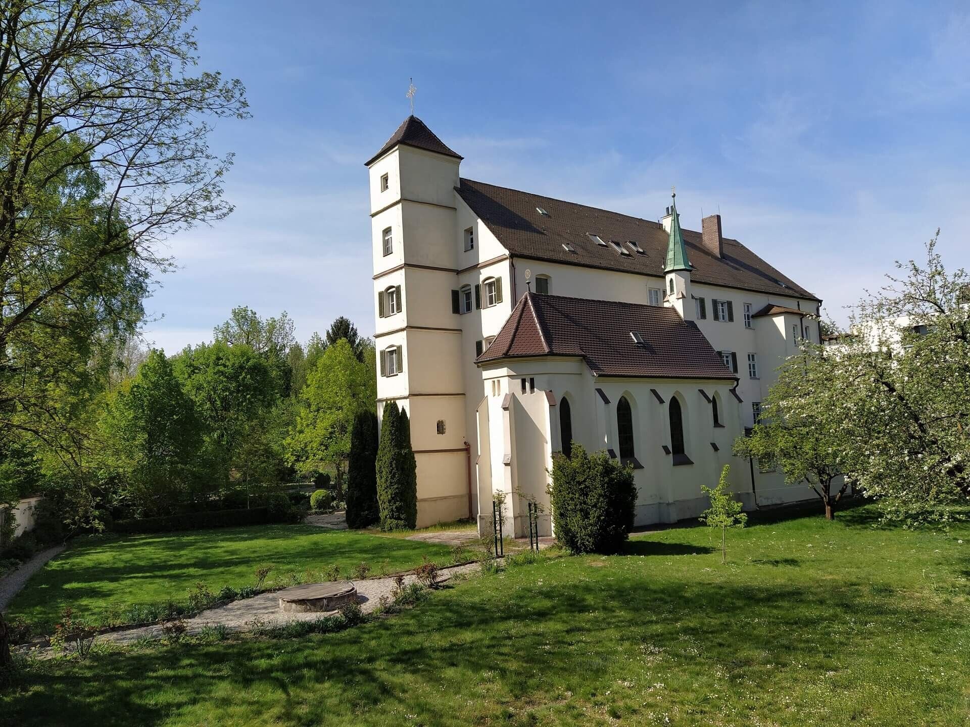 The Josefsburg in Altötting in spring, a white castle with a tower and a chapel, surrounded by a lawn