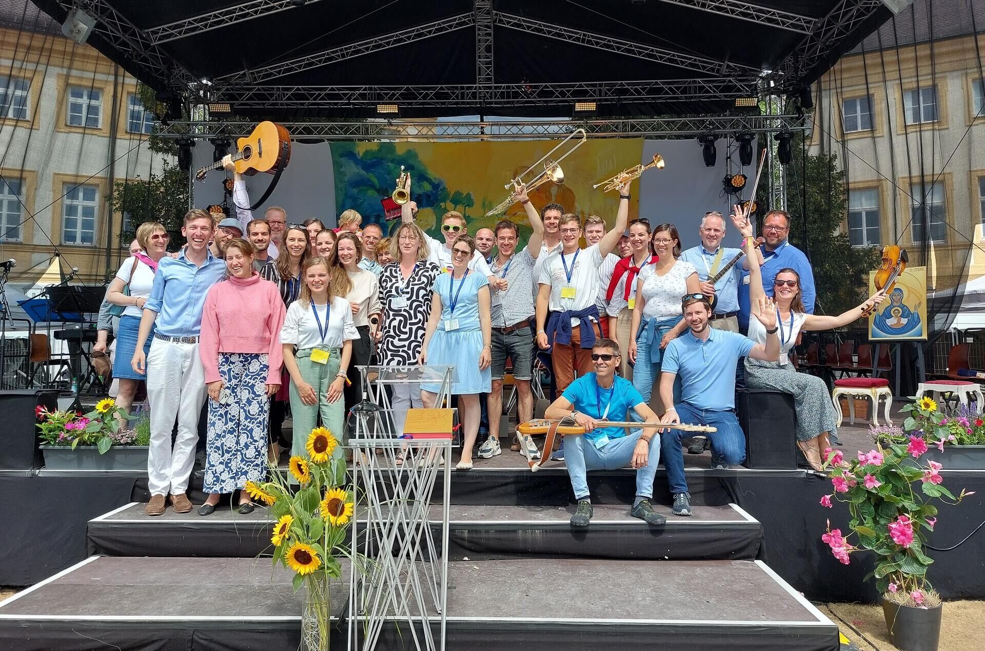 A large group of young people celebrating on an open-air stage decorated with sunflowers
