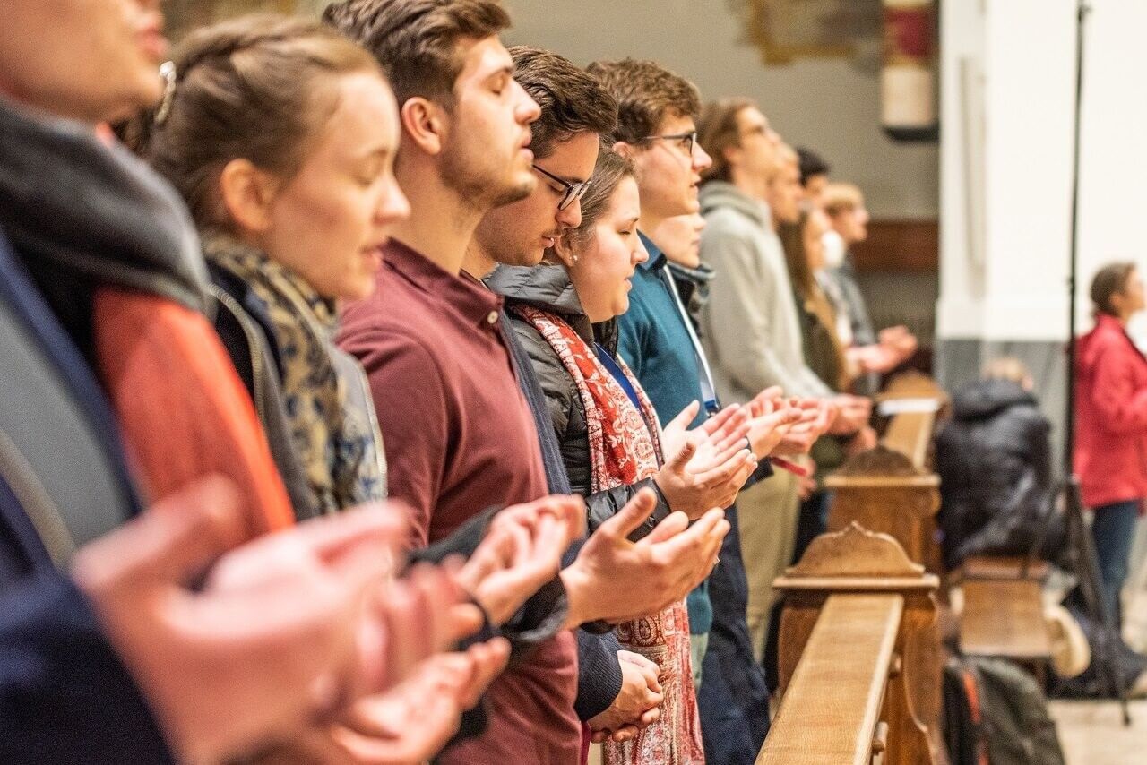 Young people praying with open hands in a church pew